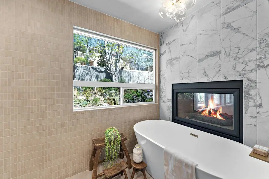 Grand Vista freestanding tub beside marble fireplace and garden window