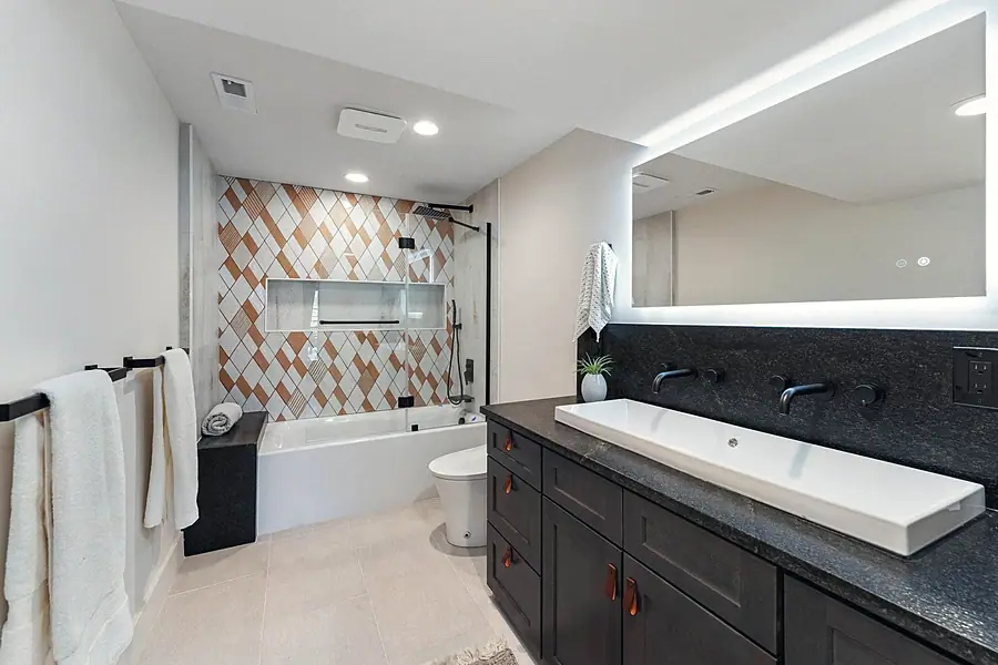Fairway House primary bath with diamond tile shower, dual wall faucets, and lit mirror
