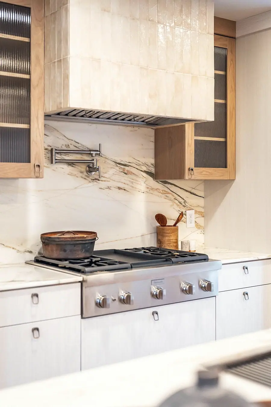 Grand Vista cooking wall with tiled range hood, marble backsplash, and wood cabinetry