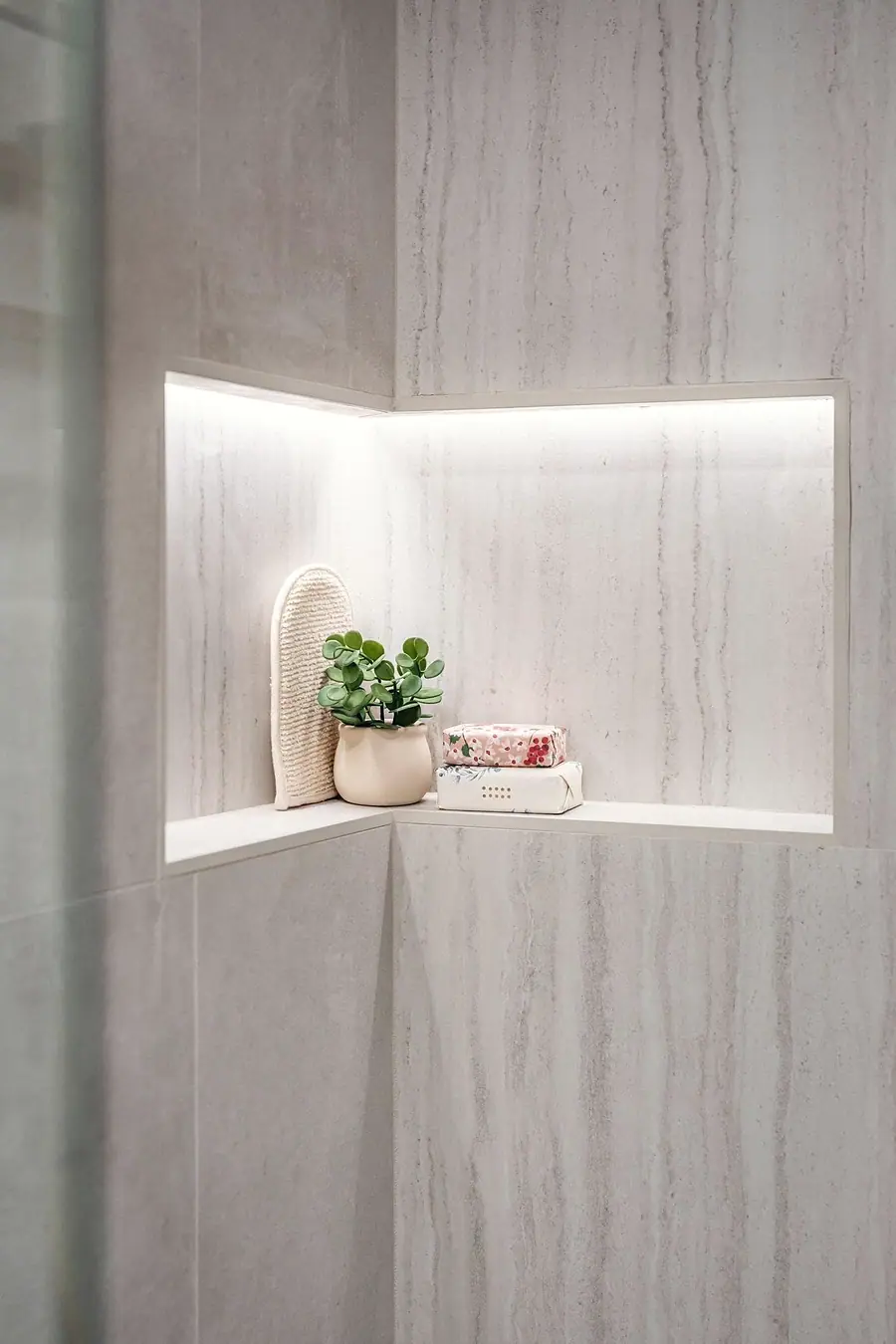 Grand Vista shower niche with LED lighting, marble tile, plant, and soaps