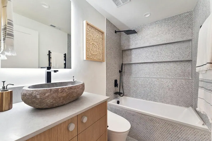 Bathroom with stone vessel sink, honeycomb tile tub surround, and black fixtures