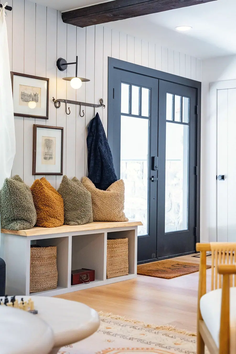 Little Gem entry with black French doors, wood bench, and bouclé pillows
