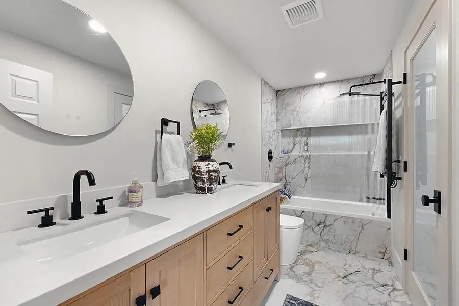 Crista da Montanha dual vanity with light oak cabinets, black fixtures, and round mirrors