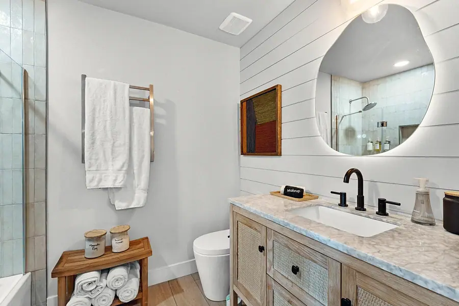 Midway bathroom with organic backlit mirror, cane vanity, and heated towel rack