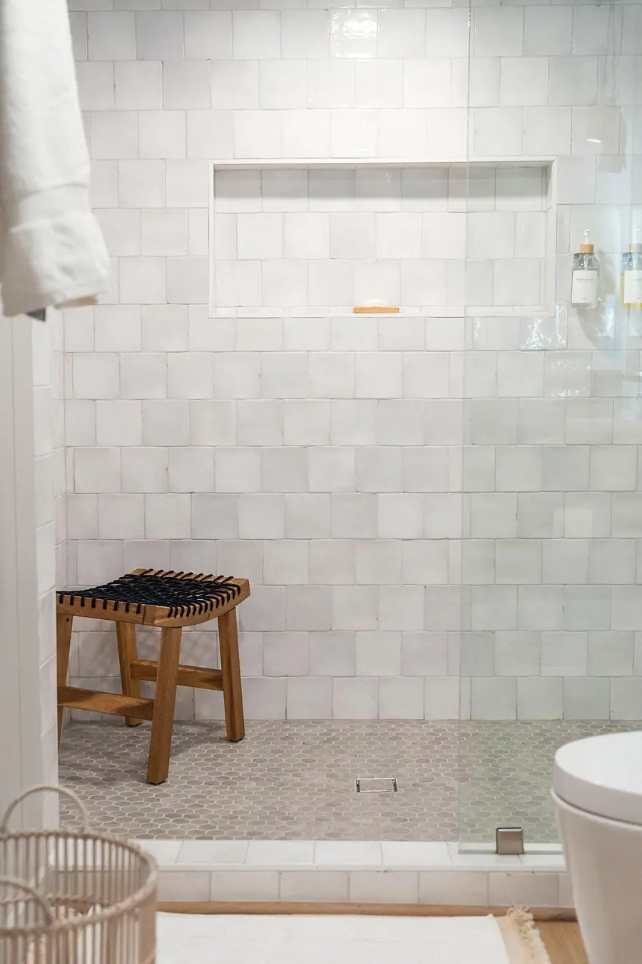 Midway walk-in shower with white square tile, woven stool, and hex floor