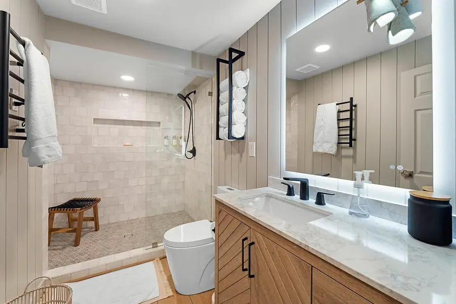 Midway bath with walk-in shower, wood chevron vanity, and backlit mirror