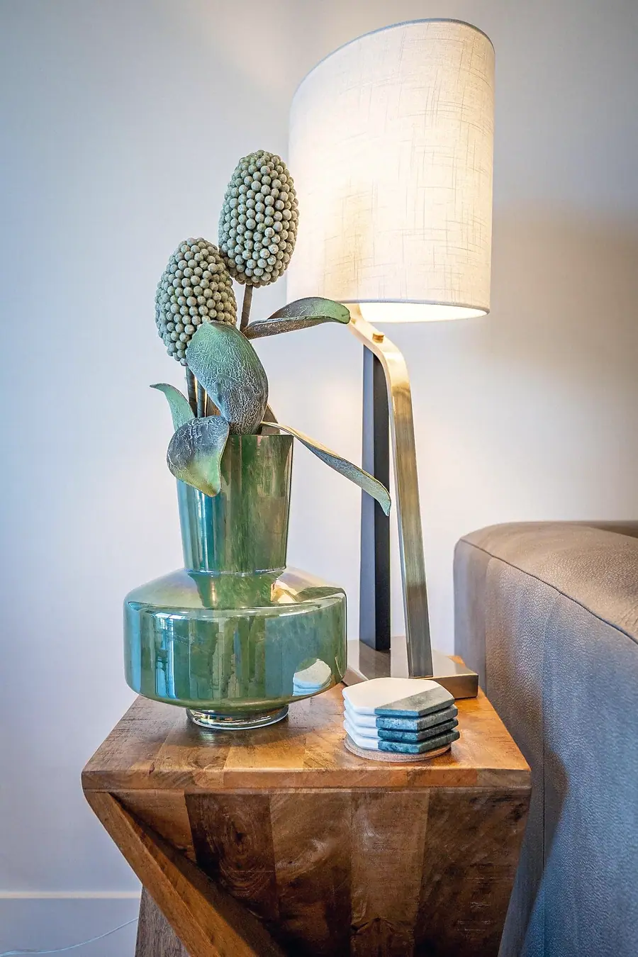 Silver Creek side table with green glass vase, sculptural stems, and modern lamp
