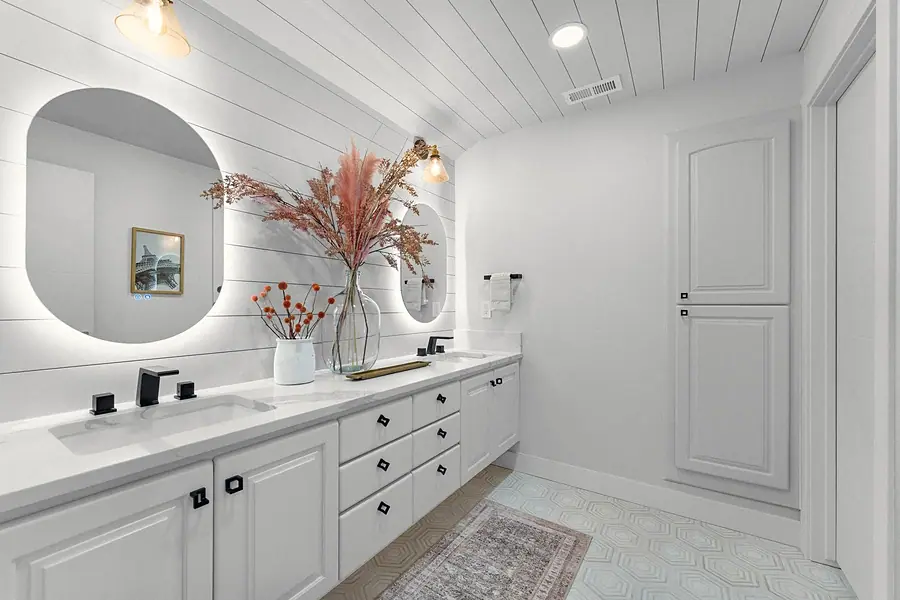 Grand Vista white bath vanity with backlit oval mirrors, black fixtures, and shiplap wall