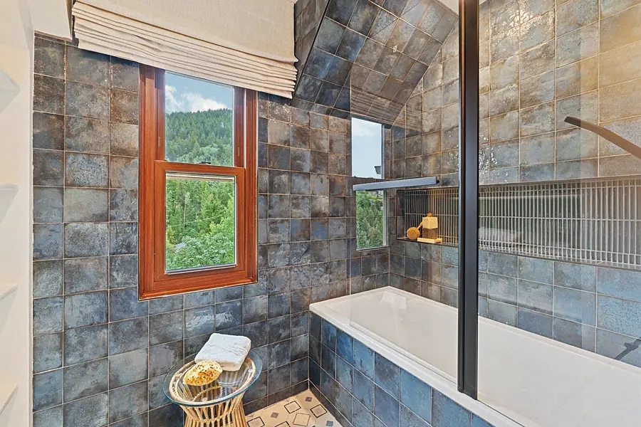 Matterhorn Hygge House spa bath with blue glazed tile walls, soaking tub, and forest window