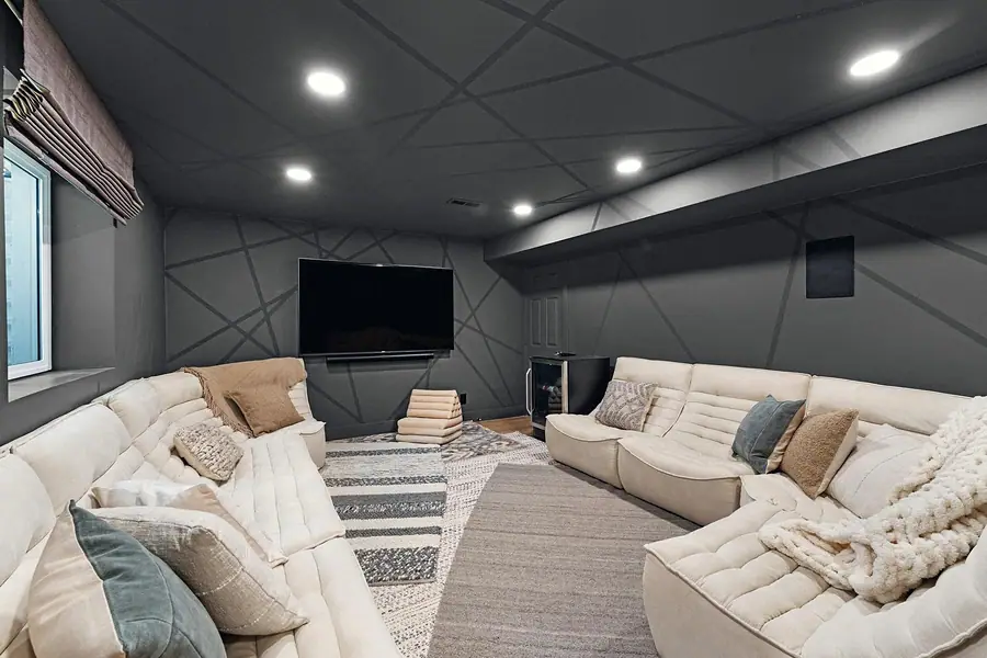 Midway media lounge with cream sectionals, geometric ceiling, and wall TV