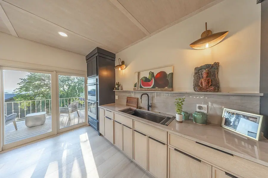 Kitchen sink wall with light oak cabinets, brass sconces, and balcony doors