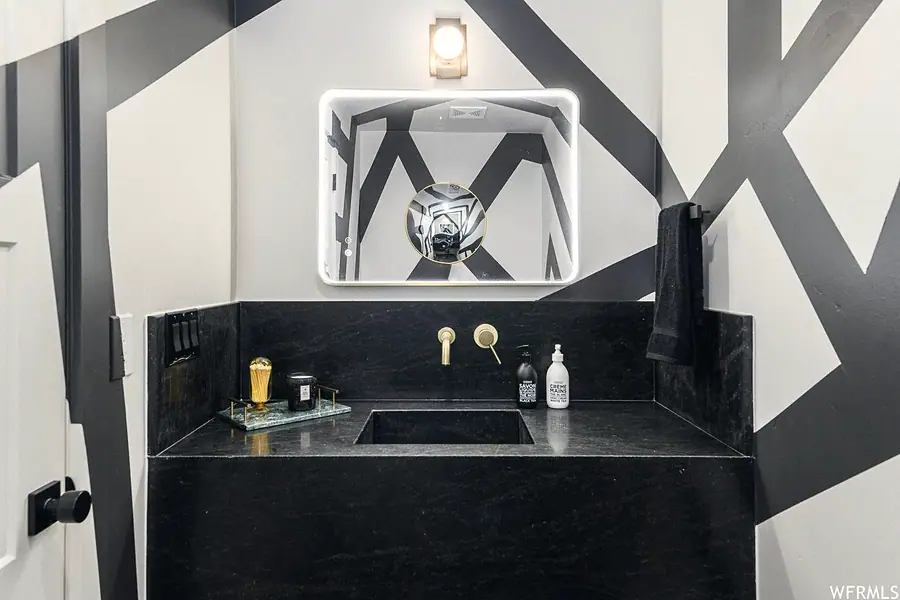 Matterhorn Hygge House powder room with lit mirror, black stone sink, and bold graphic walls