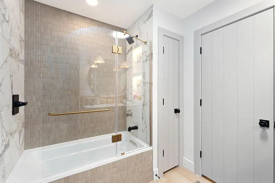 Little Gem bath with glass tub enclosure, beige tile, and marble walls