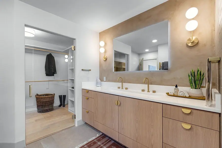 Grand Vista primary vanity with light wood cabinets, brass fixtures, and walk-in closet beyond