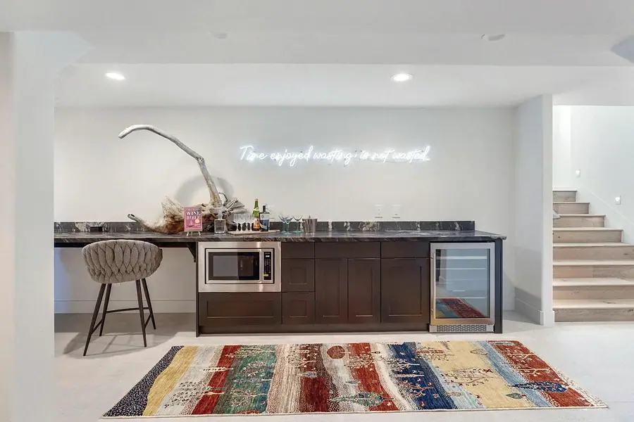 Lower-level wet bar with dark cabinetry, wine fridge, and neon sign