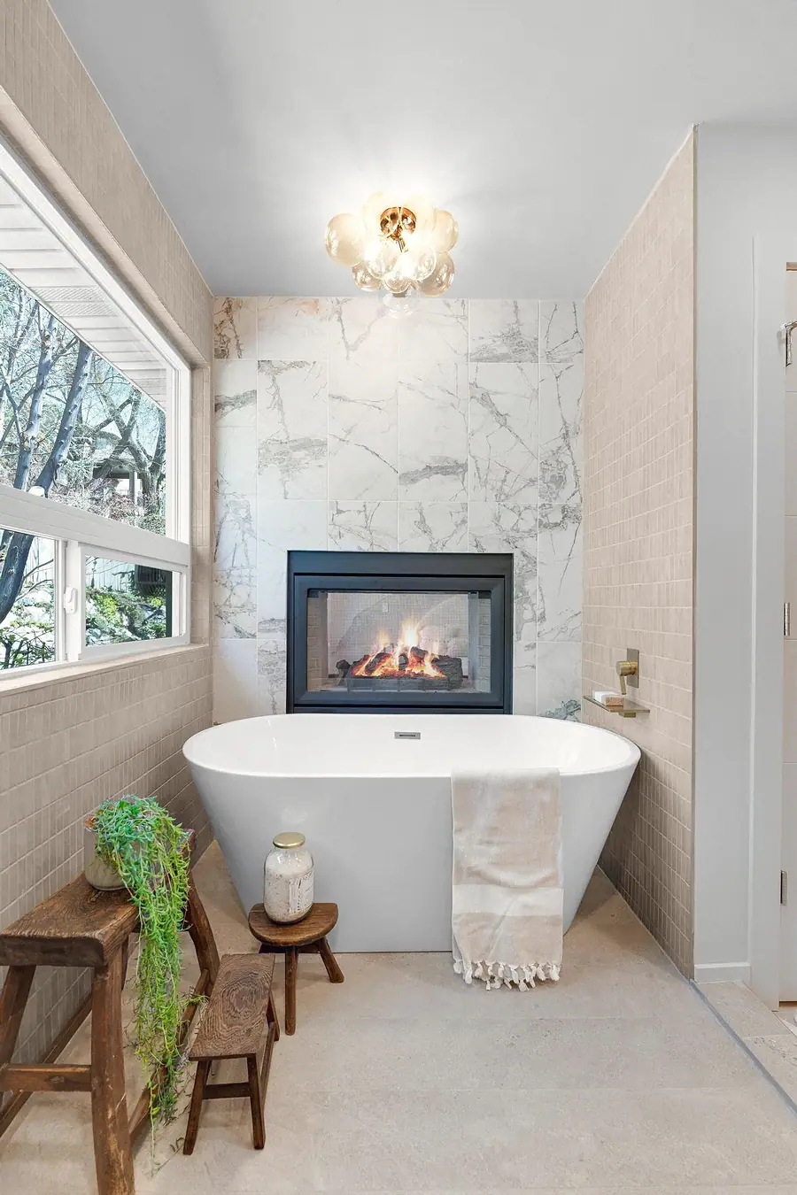 Grand Vista freestanding tub with marble fireplace wall, bubble chandelier, and garden window