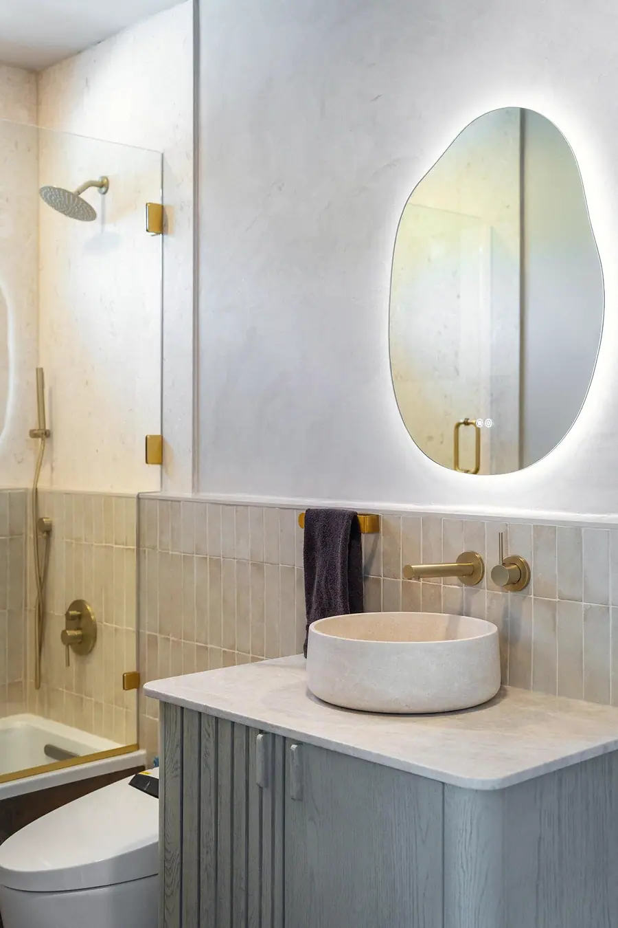 Elysium vanity detail with stone vessel sink, brass faucet, and backlit mirror