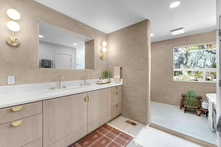 Grand Vista primary bath with dual oak vanity, brass fixtures, and walk-in shower beyond