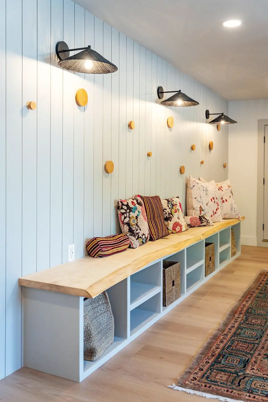 Little Gem mudroom bench with floral pillows, wood pegs, and woven baskets