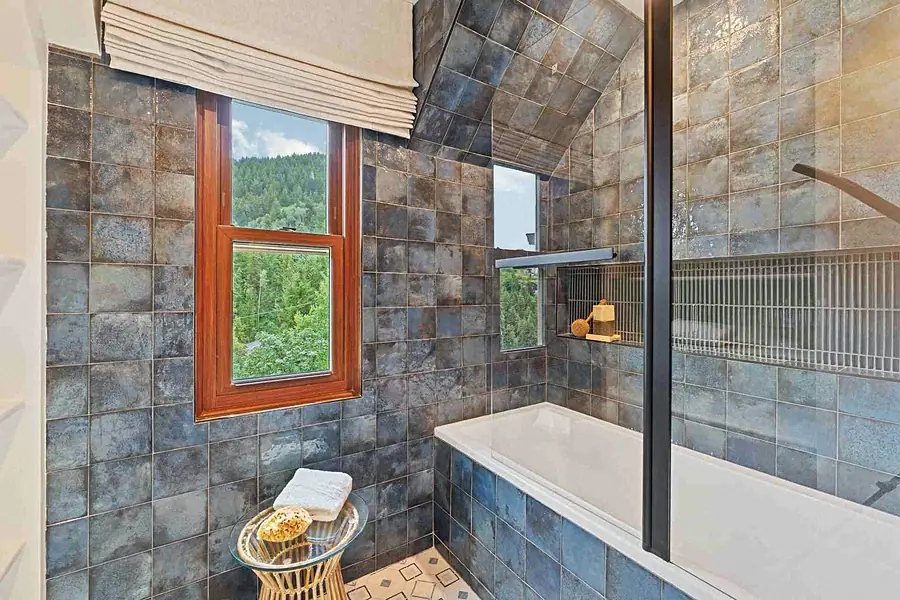 Matterhorn Hygge House spa bath with blue glazed tile walls, soaking tub, and forest window