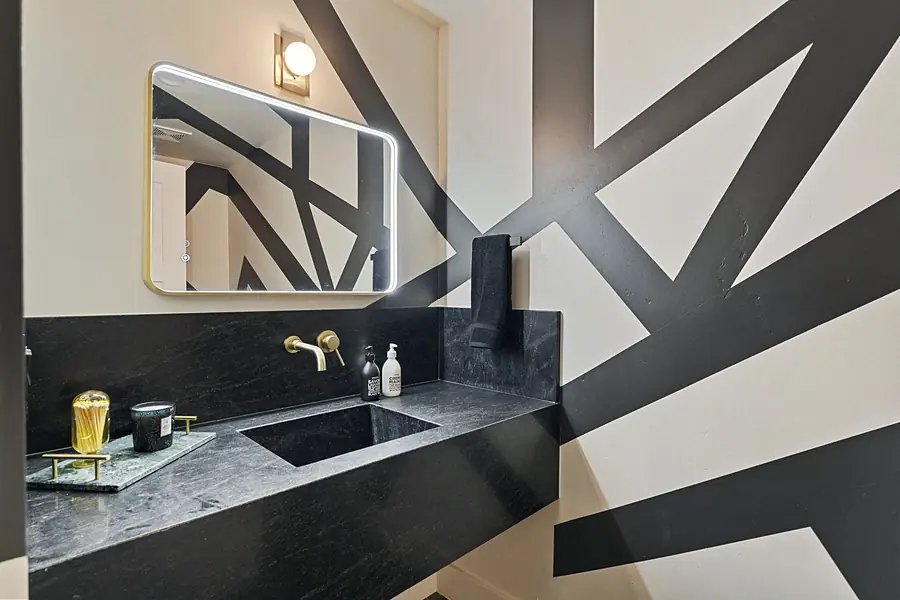 Matterhorn Hygge House powder room with black marble vanity, brass fixtures, and geometric wall mural