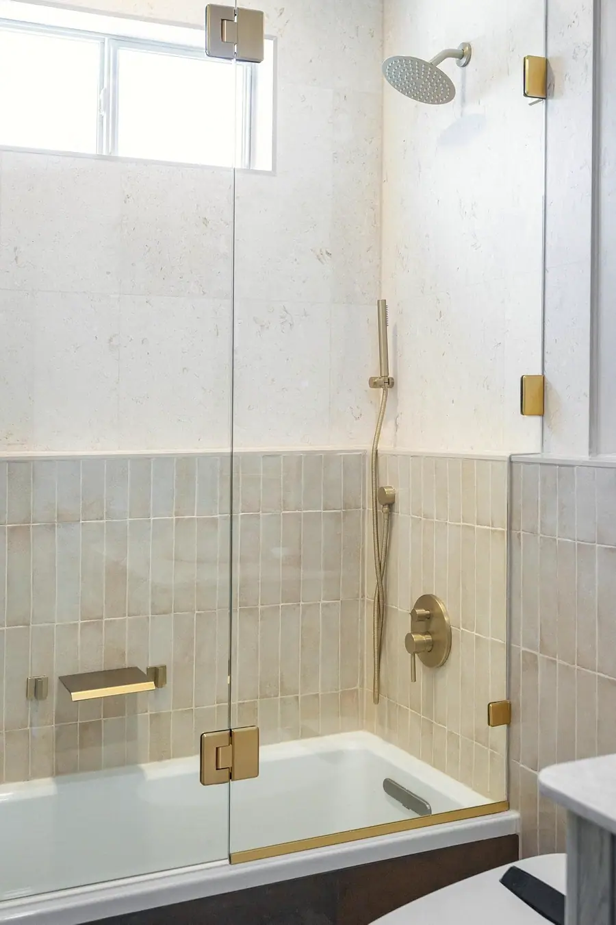 Elysium tub shower with cream tile, brass fixtures, and glass enclosure