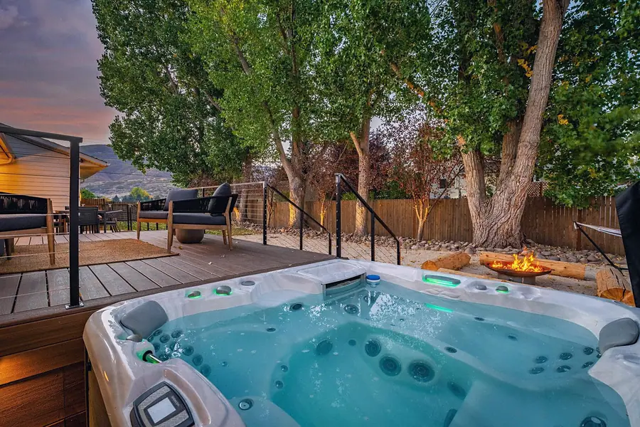 Midway hot tub at dusk with green lights, fire pit, and deck lounge beyond