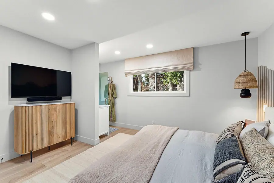 Midway primary bedroom with wall-mounted TV, fluted wood cabinet, and woven pendant