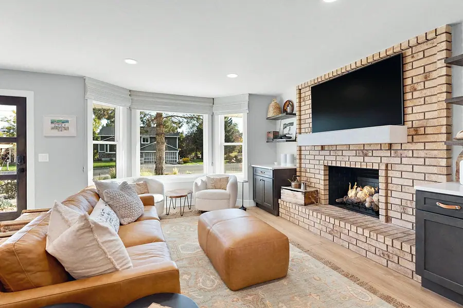 Midway living room with leather sofa, ottoman, bay windows, and brick fireplace wall