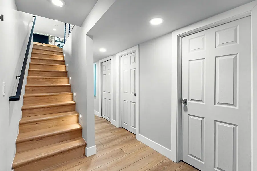 Midway lower hall with oak staircase, step lights, and white paneled doors