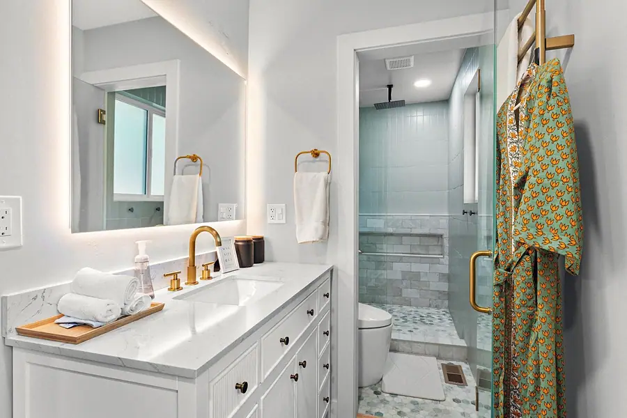 Midway bath with gold fixtures, white vanity, glass shower, and patterned robe