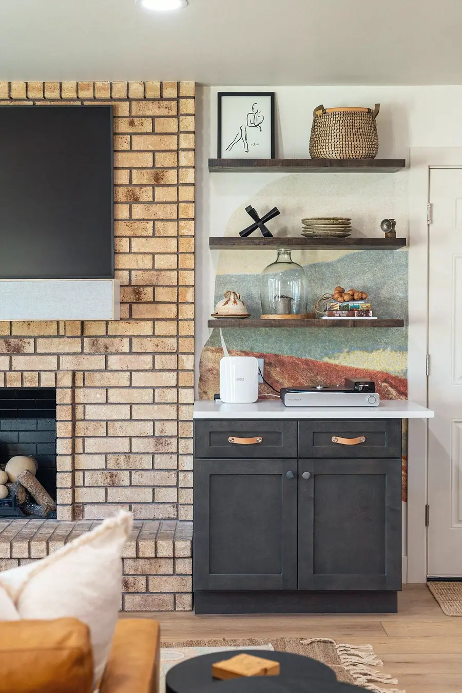 Midway living room media wall with brick fireplace, dark cabinet, and curated shelves